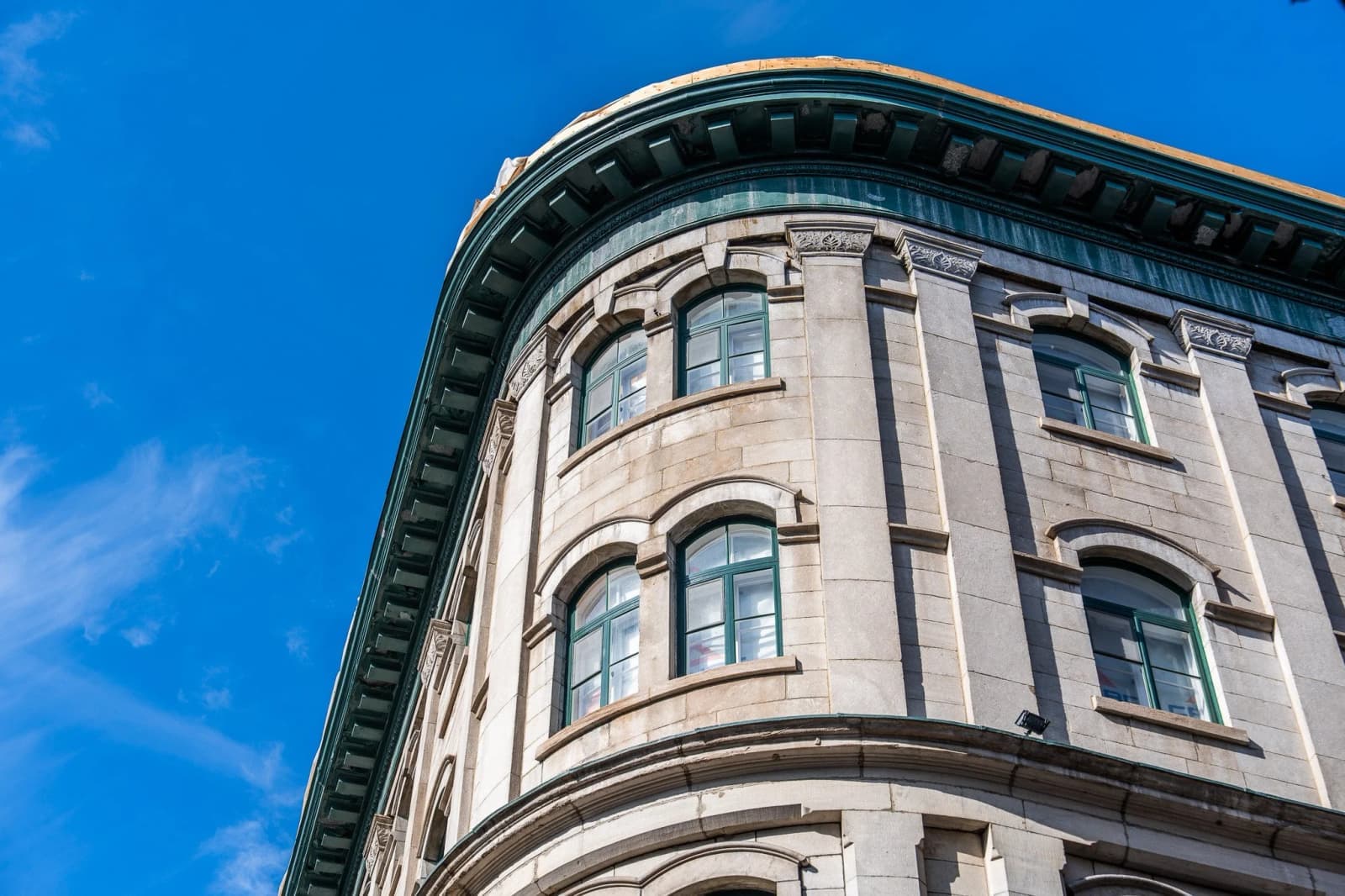 The curved stone corner of a building in Quebec City rises against a blue sky under a green copper cornice.